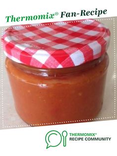 a jar filled with sauce sitting on top of a counter next to a white and red checkered table cloth