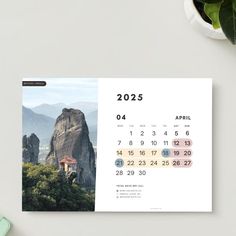 a desktop calendar with mountains in the background and greenery next to it on a desk