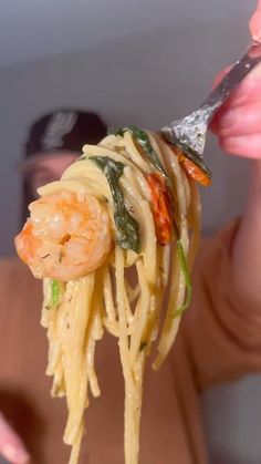 a person holding a fork full of pasta with shrimp and spinach on it's side