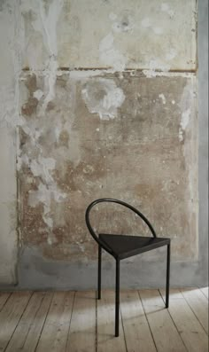 a black chair sitting in front of a wall with peeling paint on it's walls