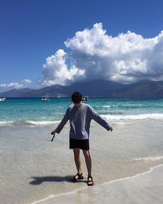 a man standing on top of a sandy beach next to the ocean under a cloudy blue sky