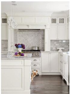 a kitchen with white cabinets and marble counter tops, along with a dog in the foreground