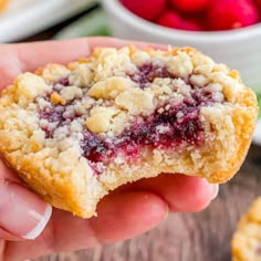 a hand holding a berry crumb cookie over a wooden table with raspberries in the background