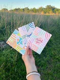 someone is holding up some cards in their hand on the grass with trees in the background