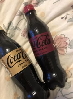 two bottles of coca cola sitting on top of a bed next to each other,