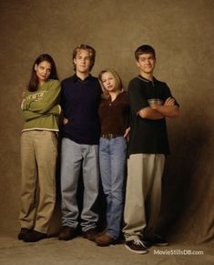 four people standing in front of a brown background with their arms crossed and looking at the camera