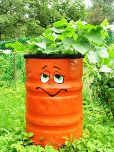 a large orange barrel with a face painted on it in the middle of some grass