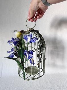 a person is holding a bird cage with flowers in it while another hand reaches for the flower