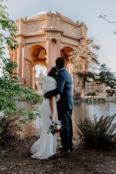 a bride and groom are standing in front of the palace at sunset with their arms around each other