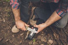 a man holding a knife in his hand while kneeling down on the ground next to some grass