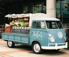 an old blue truck parked in front of a building with flowers and plants on the back