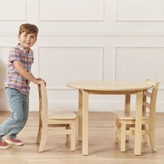 a little boy standing next to a wooden table and chair in front of a white wall