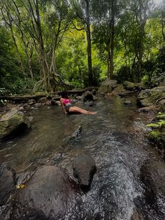 a woman laying on top of a rock in a river surrounded by trees and rocks