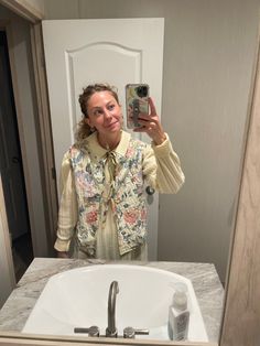 a woman taking a selfie in front of a bathroom mirror with her cell phone