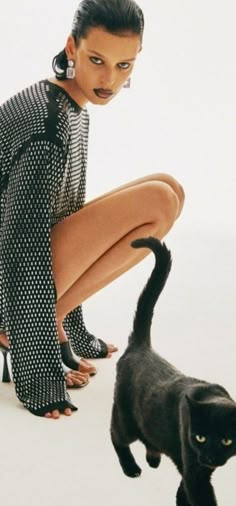 a woman kneeling down next to a black cat