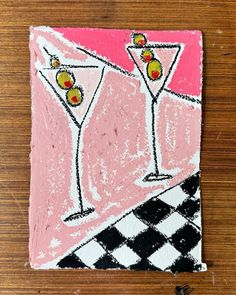 a pink and black tile with two martini glasses on it's side, sitting on a wooden surface