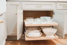 an open cabinet in a kitchen filled with dishes and bowls on the bottom shelf,