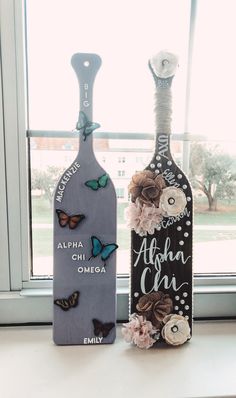 two wine bottles decorated with flowers and butterflies sitting on a window sill in front of a window