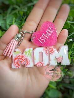 a hand holding a keychain with the word mom written on it and a pink heart