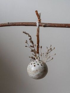 a white ball hanging from a twig on a branch with some flowers in it