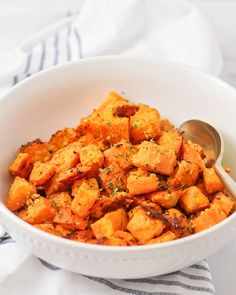 a white bowl filled with sweet potatoes on top of a striped towel next to a spoon