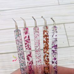 four different colored glittered toothbrushes in a person's hand