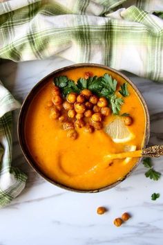 a bowl filled with carrot soup and garnished with cilantro, parsley and lemon wedges