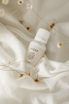 a bottle of sleep sitting on top of a white bed sheet next to some flowers