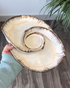 a person holding a large white plate on top of a wooden floor next to a potted plant