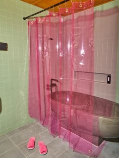 a bathroom with pink shower curtains and slippers on the floor