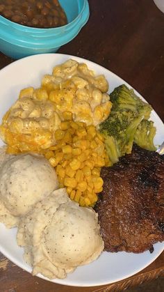 a white plate topped with meat, mashed potatoes and broccoli next to beans