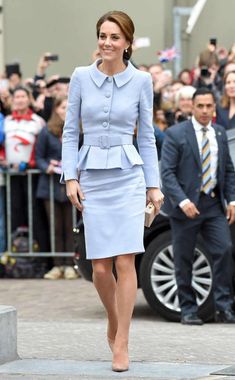 a woman in a blue dress and jacket walking down the street with people behind her