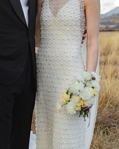 a bride and groom pose for a wedding photo in the field with mountains behind them