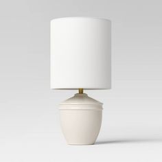 a white table lamp with a white shade on it's base and a light bulb in the middle