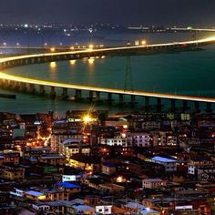 an aerial view of a city at night with lights on the buildings and water in the background