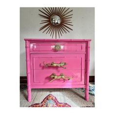 a pink dresser with gold handles in front of a sunburst on the wall