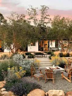 an outdoor dining area with chairs and tables surrounded by rocks, shrubs and trees in the background