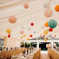 tables and chairs are set up in a tent with paper lanterns hanging from the ceiling