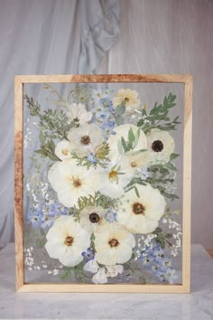 white flowers in a wooden frame on a marble countertop with blue and white flowers