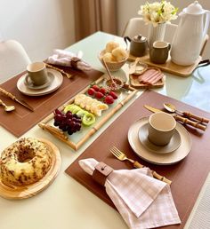 a table topped with plates and cups filled with food next to a plate covered in fruit