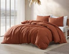 a bed with an orange comforter and pillows in a room next to a window