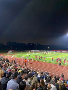 a group of people standing on top of a field next to a soccer field at night