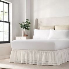 a bed with white sheets and blue ruffled bedskirt next to a window