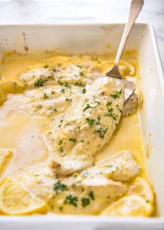 a white casserole dish filled with chicken and lemons, garnished with parsley