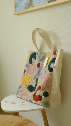 a white bag sitting on top of a wooden chair next to a wall mounted painting