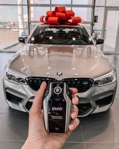 a person holding a cell phone in front of a bmw car with a bow on top