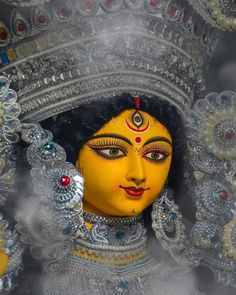 a yellow statue is surrounded by silver and red beads on it's head, in front of a gray background