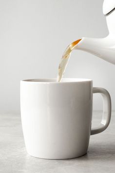 a white coffee cup filled with liquid being poured into it