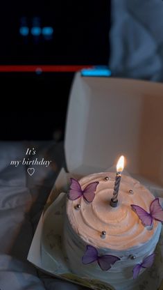 a birthday cake with white frosting and purple butterflies on it sitting in a box