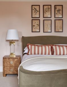 a bedroom with pink walls and pictures on the wall above the bed, along with a lamp